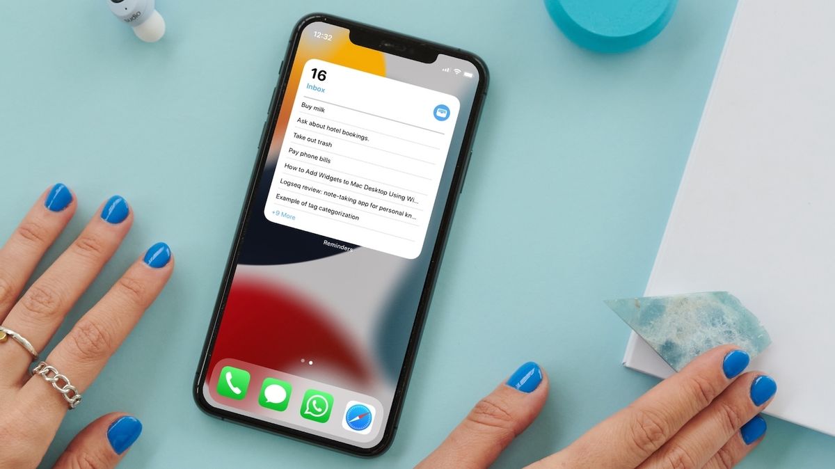 iPhone on blue table with hands on both sides showing reminders widget