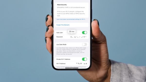 Hand holding iPhone showing the Wifi password in iOS 16