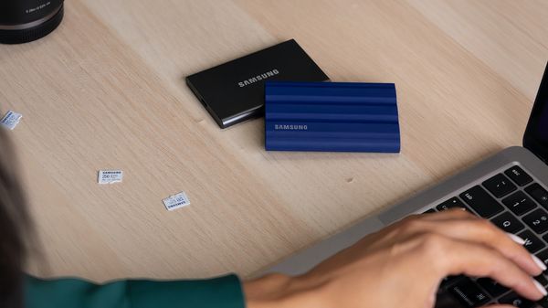 Samsung SSD and MacBook on wooden table - a person's hand is visible on MacBook keyboard