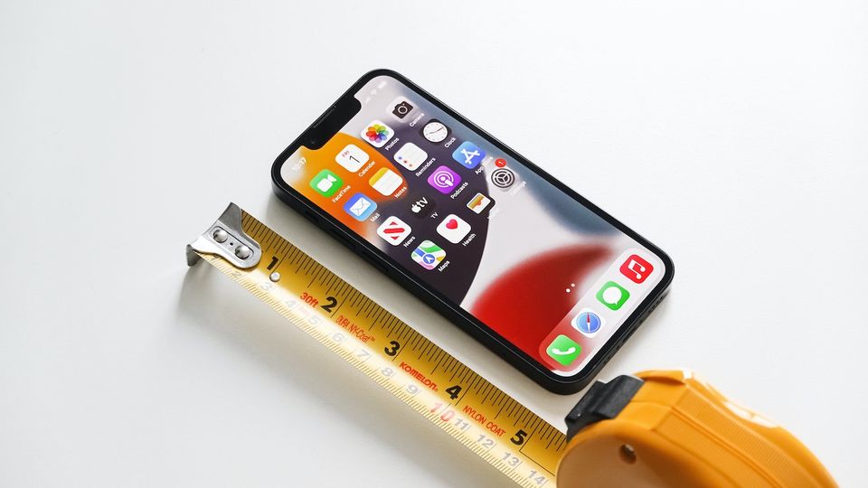 iPhone 13 mini next to a tape measure on white surface