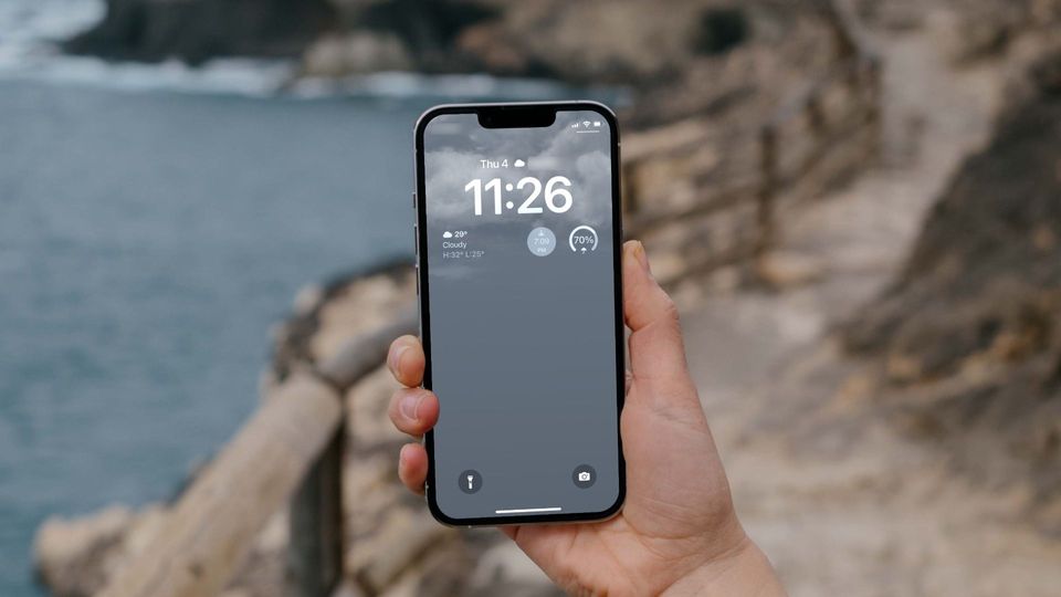 Hand holding iPhone showing dynamic weather wallpaper on Lock screen